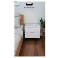 White bedside table with grey stone-patterned top beside a bed