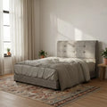 Light grey tufted bed beside a bright window