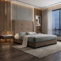 Taupe Valente bed beside tall windows at dusk